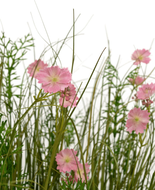 Der feuerhemmende feuerhemmende 90-cm-Kunstrasen-Zwiebelgrastopf mit rosa Gesangsblumen hat rosa Blüten mit einem hellgrünen Herzen, die zwischen hohem, dünnem Gras und üppigen Blattpflanzen blühen, alles vor einem weißen Hintergrund.