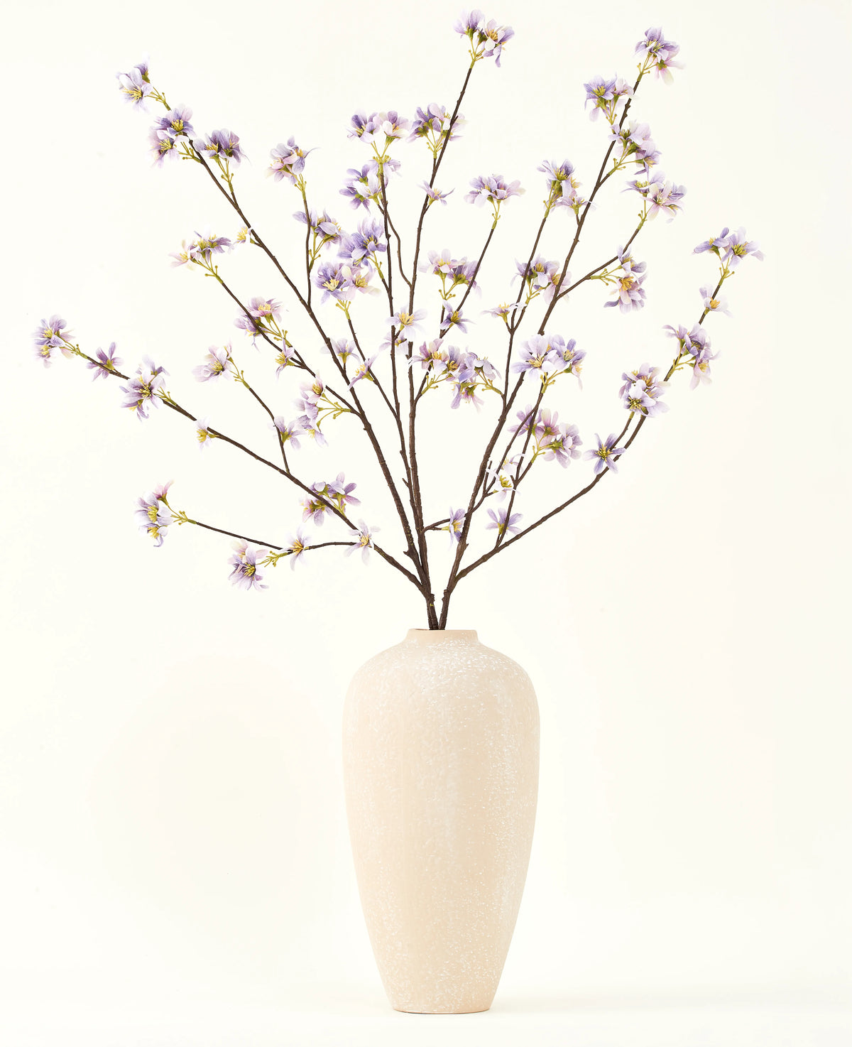 Eine hohe, cremefarbene Keramikvase enthält eine Reihe dünner Zweige mit dem Text „Seiden-Kunstblumenstrauß“ Künstlicher Blumenzweig lila, vor einem schlichten, hellen Hintergrund.