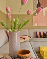 Eine 63 cm große künstliche französische Tulpe in Rosa steht in einer Vase auf dem Tisch neben einer orangefarbenen Tasse in einem gemütlichen Wohnzimmer mit einem cremefarbenen Sofa, gemusterten Kissen, einer gelben Kiste und abstrakter Wandkunst im Hintergrund.